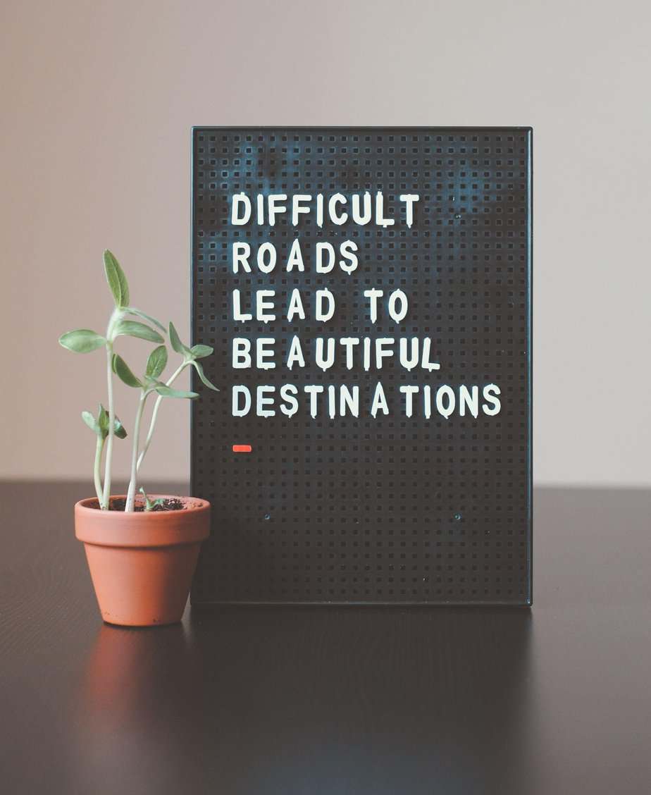 A small potted plant sits next to a black letter board displaying, “Difficult roads lead to beautiful destinations,”—a gentle reminder of hope for those on the journey of eating disorder treatment and collaborative care.