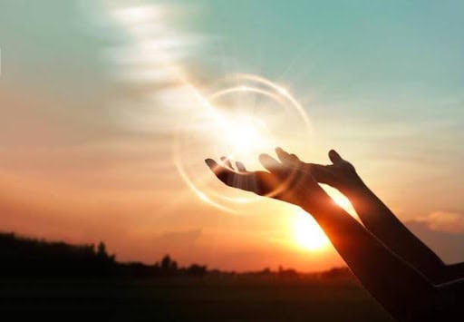 Two hands are raised toward a glowing light against a sunset sky, with rays of sunlight and lens flares creating a sense of healing and hope, symbolizing inspiration and the development of coping skills.